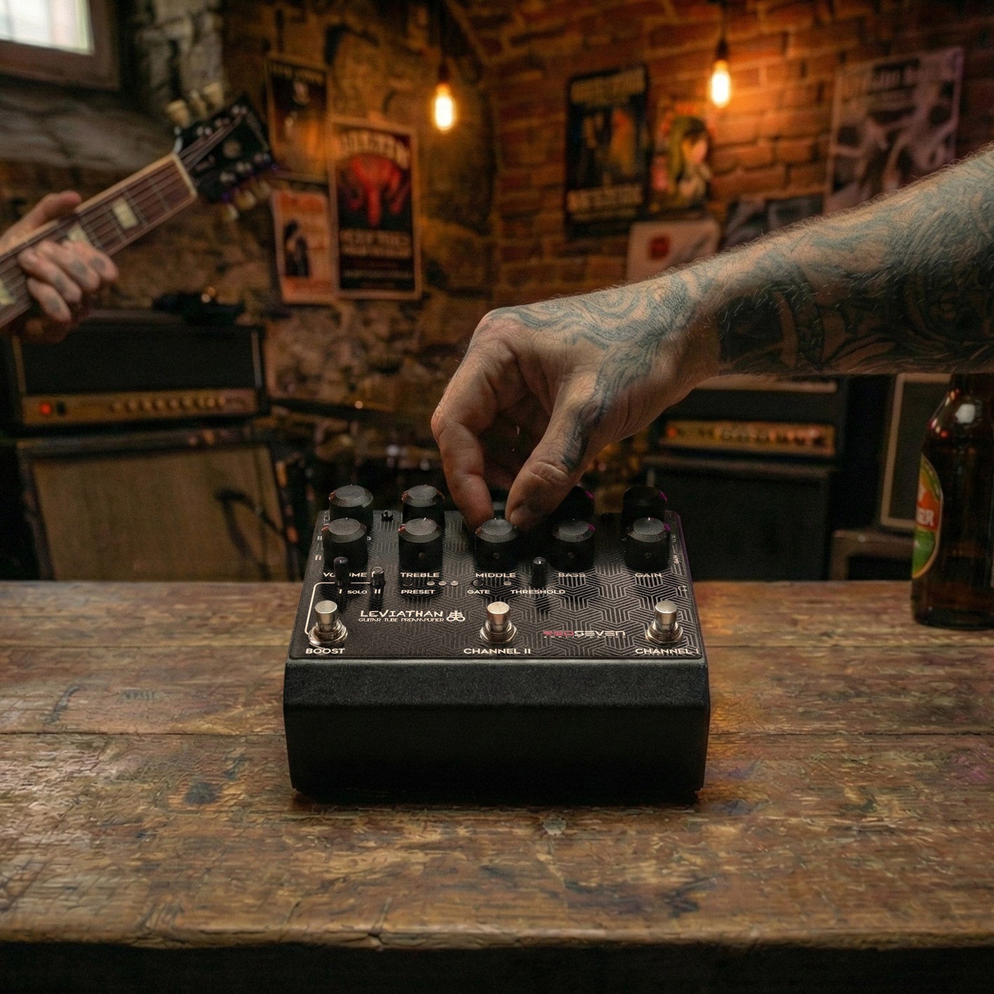 Guitarist adjusting the RedSeven Leviathan preamp pedal in a studio setting, with electric guitar and amplifiers in the background 